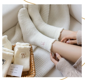 Detail of cream white fuzzy socks featuring pink embroidered bows and soft plush texture
