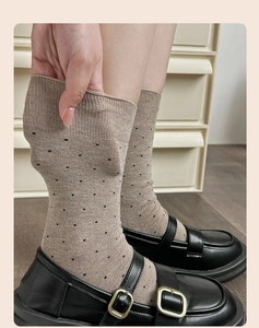 Close-up of beige wool socks with black polka dots showing elastic knit texture