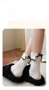 Close-up of white ribbed socks featuring grey ruffle cuffs and black bow accents