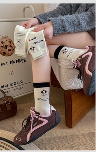 Detail view of cream mid-tube socks featuring cartoon dog design and black contrast trim