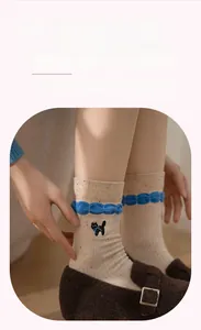 Detail of beige knit socks with cat embroidery, blue ruffle cuffs and colorful specks