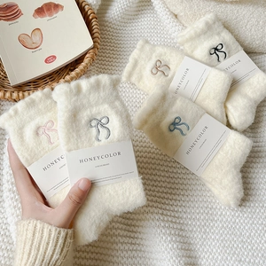 Five pairs of plush white crew socks with colorful embroidered bows on a cozy knit background