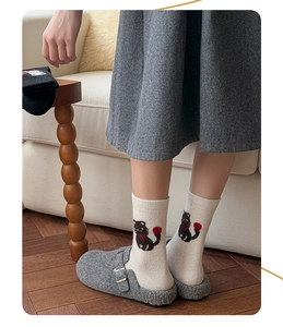Nahaufnahme von cremefarbenen Wollsocken mit Katzenmuster und grauen Filzpantoffeln