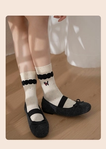 Close-up of cream crew socks with black cat embroidery and ruffled edges in soft lighting