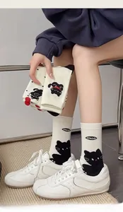 Detail of white cotton crew socks featuring black cartoon cat patterns and miao lettering