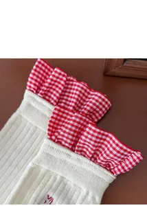 Close-up of beige ribbed knit socks with red checkered ruffle and embroidery detail