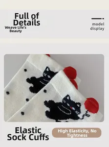 Detail of elastic cuff on beige cotton socks featuring black cat pattern and red pom-poms
