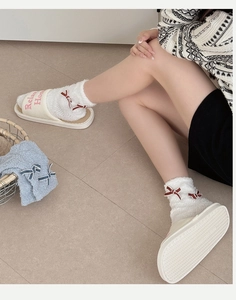 Nahaufnahme weißer Fleecesocken mit roten Schleifen und gemütlichen Hausschuhen für Damen
