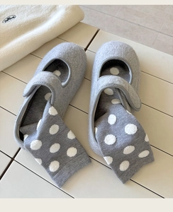 Detail of gray felt Mary Jane slippers with polka dot knit socks on a wooden surface