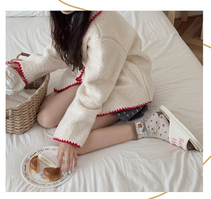 Detail of cozy off-white fleece cardigan with red wavy trim and matching slippers