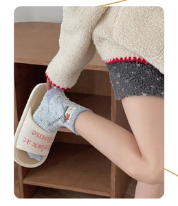 Detail of coral fleece sock with bear patch and bow tie next to plush home slippers
