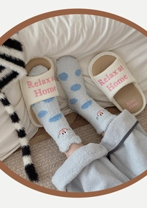 Close-up of blue polka dot coral fleece socks and beige open-toe home slippers on bed