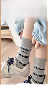 Detail of light gray striped crew socks with 'As You Wish' embroidery and white sneakers