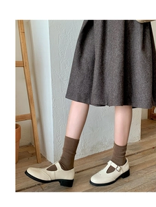 Close-up of off-white Mary Jane shoes with brogue detailing and block heels on socks