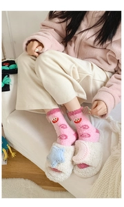 Close-up of pink coral fleece socks with cartoon face and plush white slippers