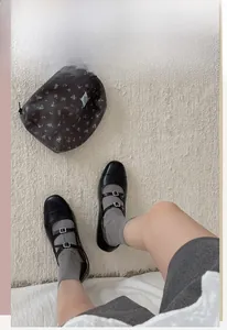 Detail of grey crew socks paired with black double-strap Mary Jane shoes on a beige carpet