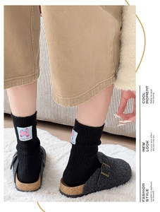 Detail of black wool socks with pink cat patch paired with grey felt mule slippers