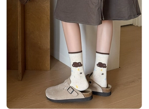 Close-up of beige cotton crew socks with cloud patterns and khaki suede mule shoes