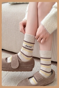 Detail of striped knitted crew socks featuring 'As You Wish' embroidery and warm color tones
