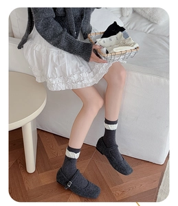 Detail of grey socks with white ruffle cuffs paired with grey Mary Jane shoes on a sofa