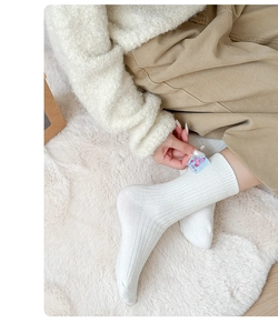 Detail of white ribbed wool socks with a blue cartoon patch on a cozy plush rug