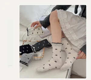 Detail of grey crew socks with black bow embroidery and ruffled cuffs on bed
