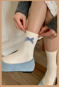 Detail of cream knit crew socks featuring a blue plaid bow accessory on the ankle