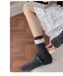 Detail of grey knitted socks with white ruffle trim and black cross-stitch embroidery details