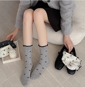 Detailed knit texture of grey crew socks featuring delicate black bow patterns and soft ribbed cuffs