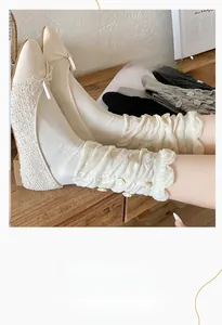 Detail of white slouch socks featuring 3D rose ornaments and ruffled cuffs on wood
