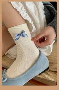 Close-up of cream cotton mid-calf socks with textured diamond patterns and blue plaid bow