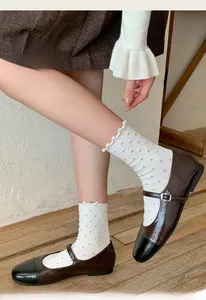 Détail de chaussettes blanches à pois gris avec bordure volantée et chaussures Mary Jane