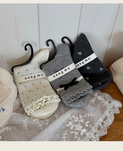 Détail de chaussettes mi-mollet grises et crème avec nœuds, pois et texture en coton côtelé