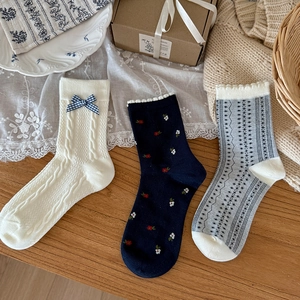Three pairs of navy and floral patterned cotton socks with bows in a cozy home setting
