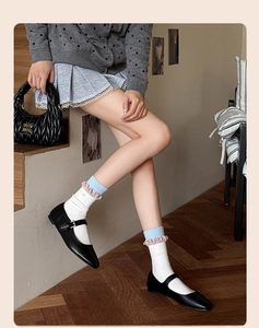 Detail of white cotton socks with pastel blue and pink ruffled edges worn with black shoes
