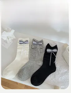 Three pairs of ballet-style crew socks with ribbons and plaid bows in cream, grey, and black