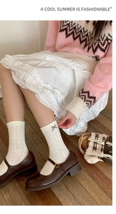Detail of white knit crew socks with hollow patterns and a metal cross charm accessory
