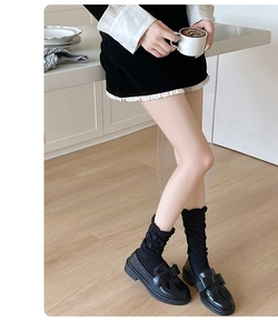 Detail of black loafers with bows and ruffled loose socks on wooden floor
