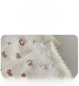 Detail of white knit sock featuring red bow embroidery and elegant lace trim with pearls