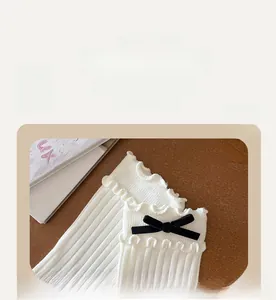 Close-up of white ribbed crew socks with double ruffle edges and black velvet bows