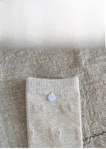 Detail view of beige ribbed socks with butterfly pattern and decorative blue button