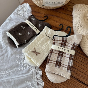 Three pairs of vintage floral and plaid cotton socks with bows on a rustic wooden desk