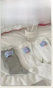 Detail of ribbed cotton socks with lace trim and brand tags on a cozy white bed