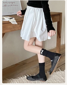Detail of ballet style socks with white X patches and black bow flat shoes on a rug