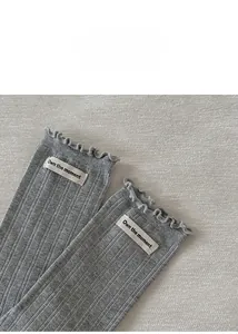 Détail de chaussettes en maille grise avec bordure ondulée et étiquette en tissu brodé
