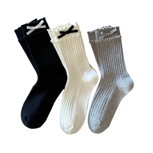 Three pairs of ballet-style ribbed crew socks with ruffles and velvet bows in black, white, and grey