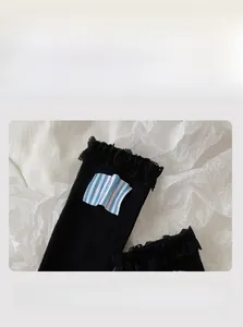Close-up of elastic lace cuff and blue striped letter tag on black cotton crew socks