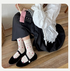 Detail of white Fair Isle crew sock with red heart patterns and Mary Jane shoes