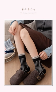 Close-up of black and white striped socks with gray accents and brown clogs on wood floor