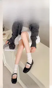 Dettaglio degli scaldamuscoli in maglia bianca con scarpe Mary Jane nere e gonna corta